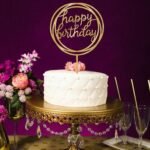 Person with birthday cake topper Australia Gold color, front view, showing “Happy Birthday” text.