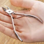 Person with stainless steel nail clipper Australia Silver color, front view, showing curved edge.