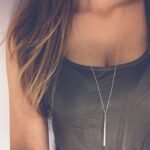 Person with stick necklace Australia Gold color, front view, showing hollow pendant.